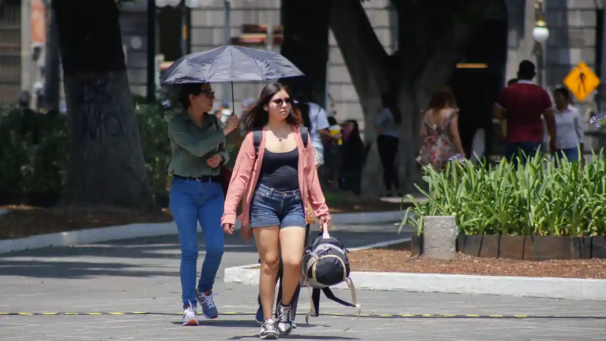 ¿A cuántos grados estamos hoy en Puebla? mujeres caminando en el Zócalo de Puebla con una sombrila y ropa ligera.