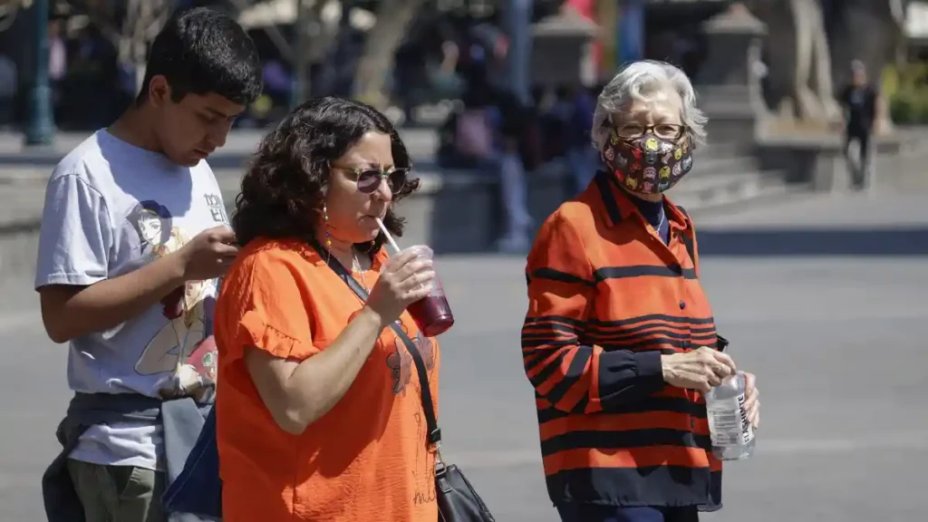 Mujeres y un adolescente caminando por el Zócalo de Puebla tomando bebidas refrescantes por el calor.