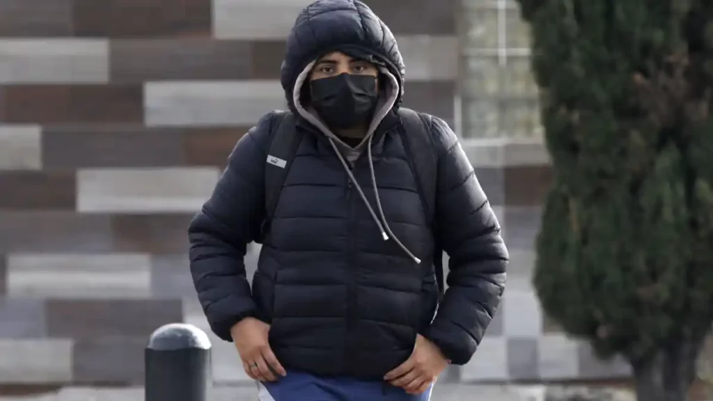 Joven abrigado y usando cubrebocas caminando por las calles de Puebla.